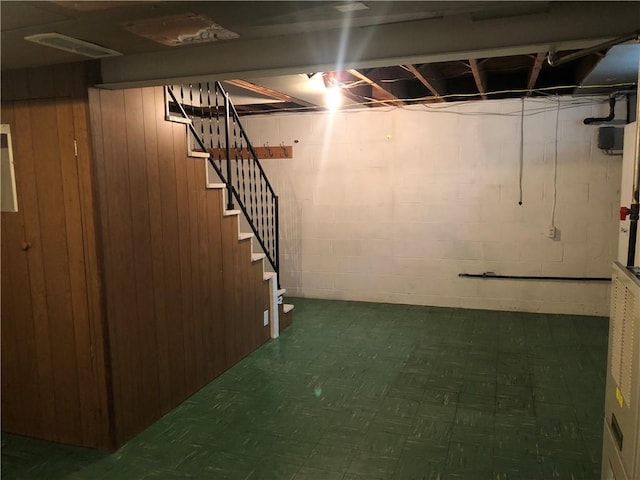 unfinished basement with tile patterned floors, wooden walls, stairs, and concrete block wall