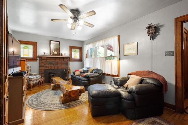 living room with plenty of natural light, wood finished floors, a ceiling fan, and a brick fireplace