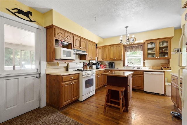 kitchen with white appliances, under cabinet range hood, brown cabinets, a chandelier, and dark wood-type flooring