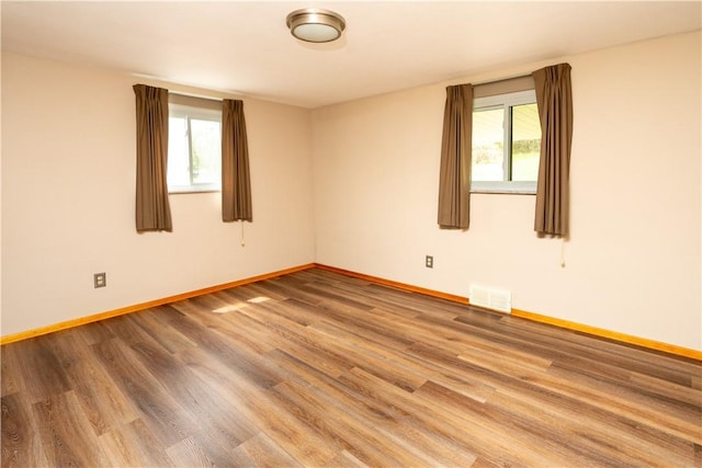 unfurnished room featuring plenty of natural light, baseboards, and wood finished floors