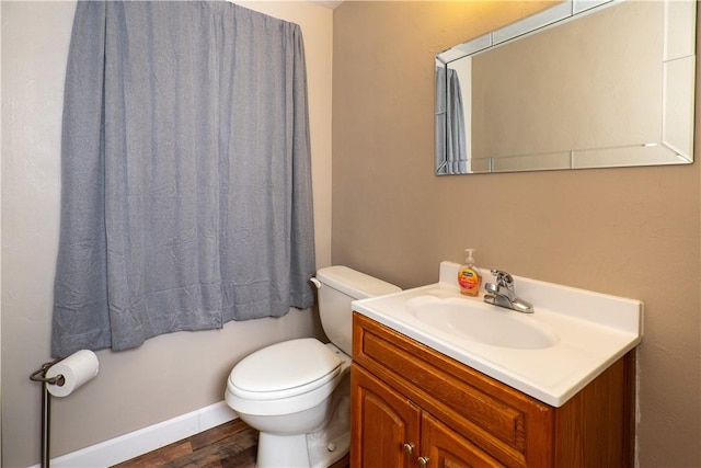 half bathroom with wood finished floors, toilet, vanity, and baseboards