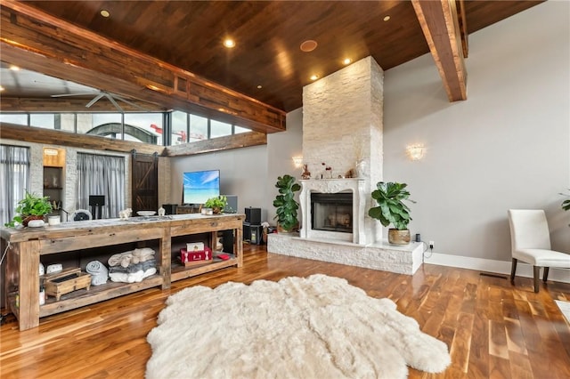 living room featuring wood ceiling, baseboards, a stone fireplace, wood finished floors, and beamed ceiling