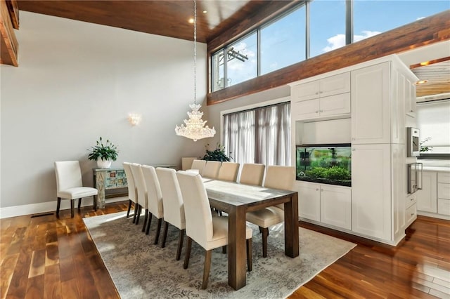 dining room with a high ceiling, dark wood-type flooring, a chandelier, and baseboards