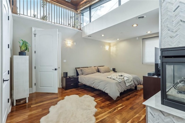 bedroom with wood finished floors, a towering ceiling, and a multi sided fireplace