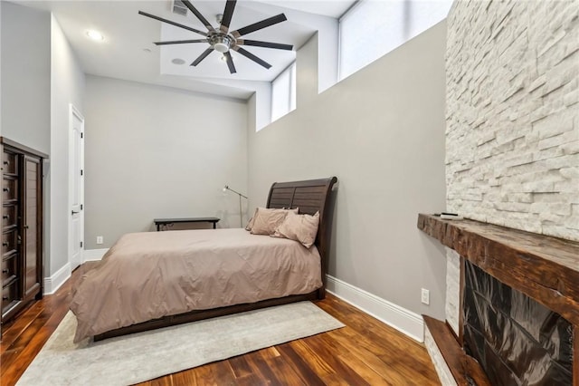bedroom with dark wood-style floors, a towering ceiling, baseboards, and a large fireplace