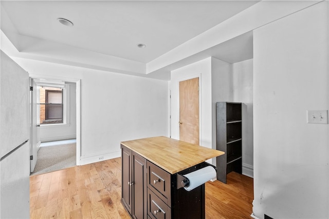kitchen with butcher block counters, a raised ceiling, light wood-style floors, and baseboards