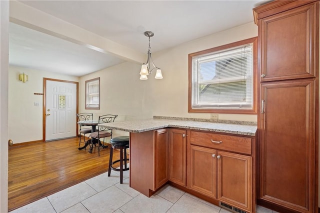 9235 Mary Ave, Mccandless, PA 15237 - kitchen featuring brown cabinets, a kitchen breakfast bar, light stone counters, light tile patterned flooring, and pendant lighting
