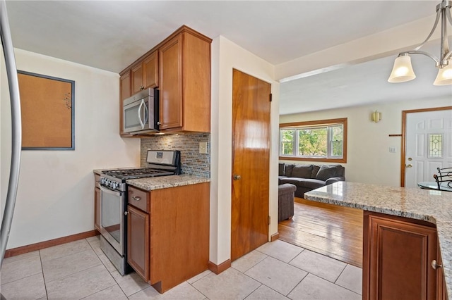 9235 Mary Ave, Mccandless, PA 15237 - kitchen featuring appliances with stainless steel finishes, brown cabinets, light stone countertops, light tile patterned floors, and baseboards