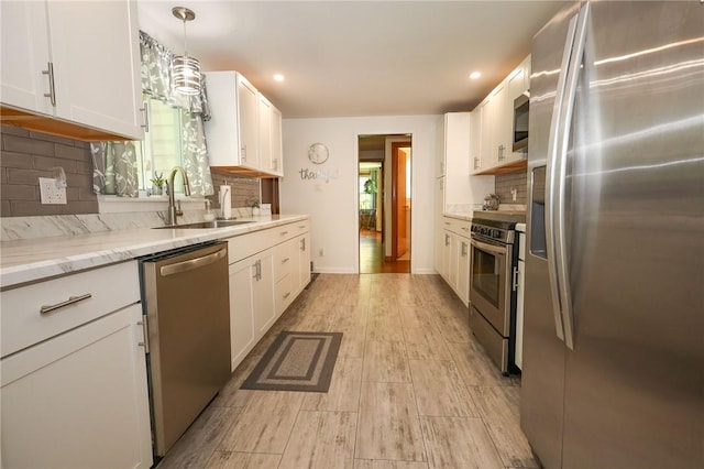 kitchen featuring appliances with stainless steel finishes, a sink, white cabinetry, backsplash, and light wood-style floors