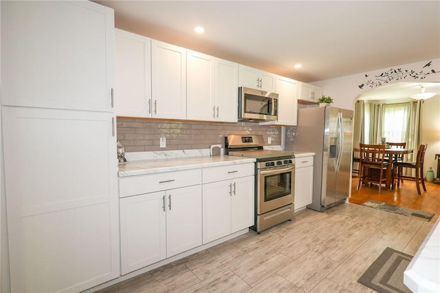 kitchen with appliances with stainless steel finishes, light countertops, white cabinets, decorative backsplash, and light wood finished floors