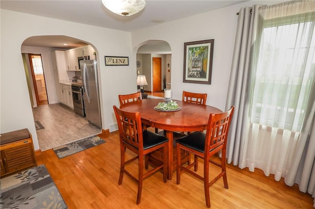 dining area featuring arched walkways and light wood-type flooring