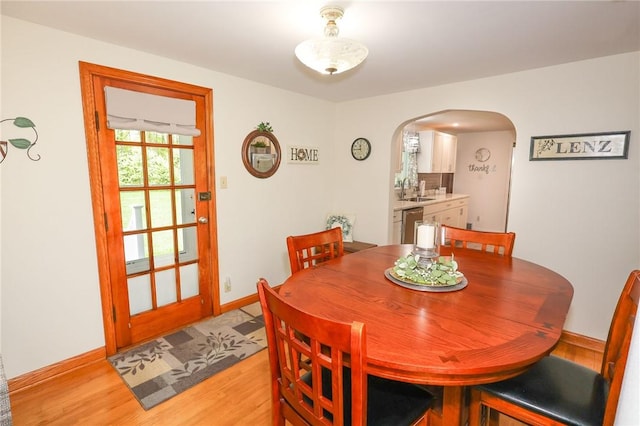 dining area with arched walkways, light wood-style flooring, and baseboards