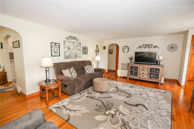 living area with arched walkways, wood finished floors, and baseboards