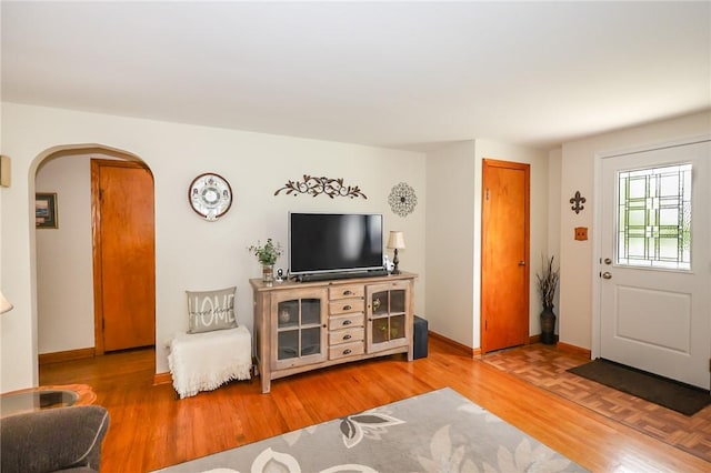living area featuring arched walkways, baseboards, and light wood finished floors
