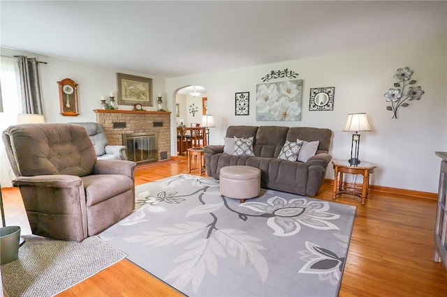 living area featuring arched walkways, a brick fireplace, light wood-type flooring, and baseboards