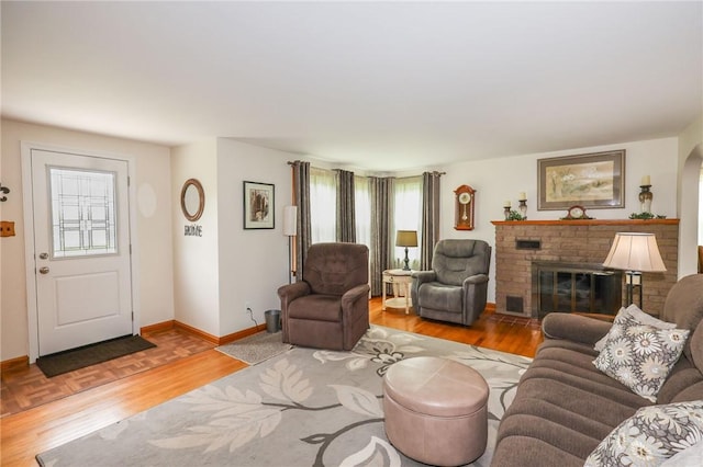 living room featuring a brick fireplace, baseboards, and wood finished floors