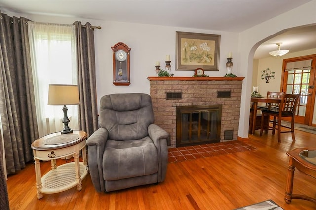 sitting room with arched walkways, a fireplace, and wood finished floors