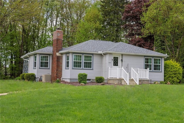 view of front of home with a chimney, a front lawn, a shingled roof, and central AC