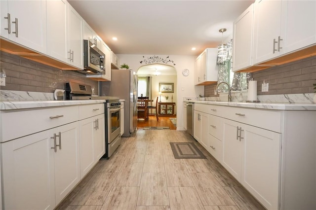 kitchen with stainless steel appliances, arched walkways, white cabinets, decorative backsplash, and recessed lighting