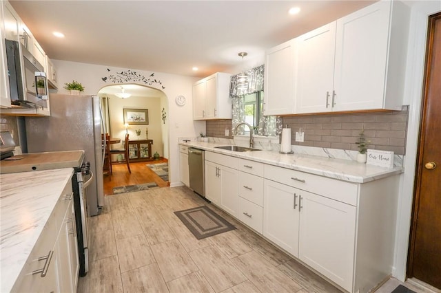 kitchen featuring appliances with stainless steel finishes, a sink, arched walkways, white cabinetry, and decorative backsplash