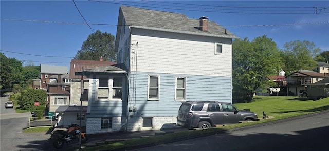 view of side of property with a chimney, a lawn, and a shingled roof