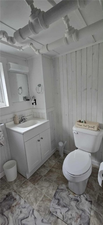 half bathroom featuring toilet, wooden walls, and vanity