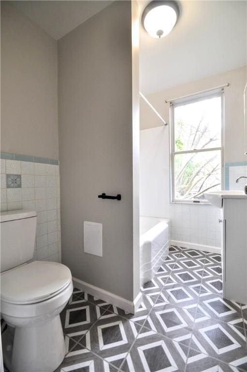 full bathroom with tile walls, toilet, a wainscoted wall, bathtub / shower combination, and vanity