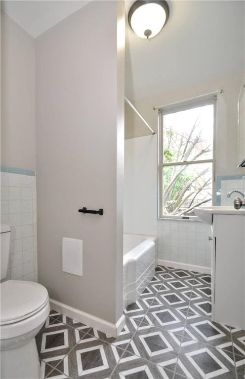 full bath with tile walls, toilet, vanity, tub / shower combination, and wainscoting