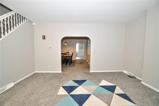 carpeted spare room featuring arched walkways, stairs, and baseboards