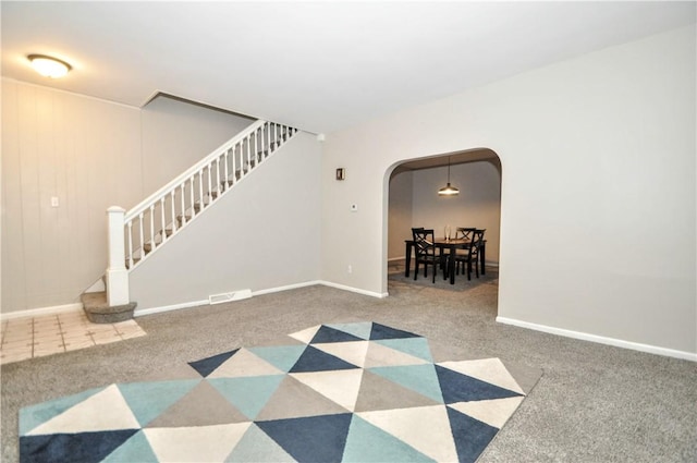 empty room featuring arched walkways, carpet flooring, stairway, and baseboards