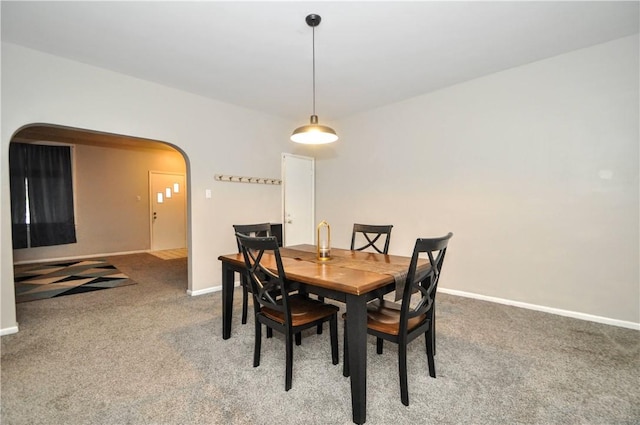 dining space featuring arched walkways, light carpet, and baseboards