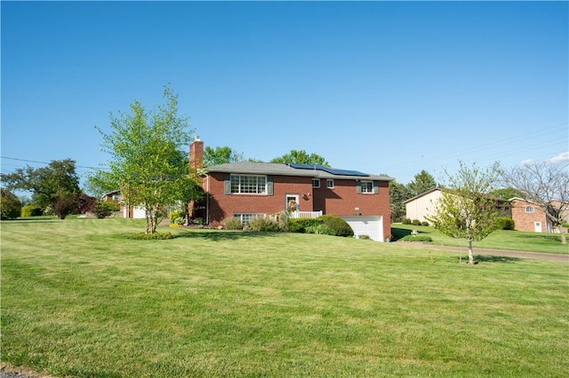 back of property with a garage, solar panels, a chimney, and a yard