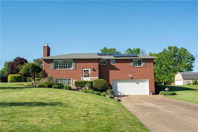 bi-level home with a chimney, a front yard, solar panels, driveway, and a garage