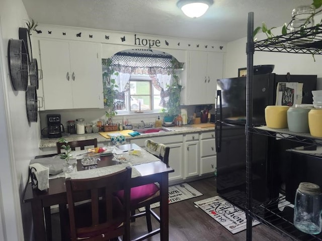 kitchen featuring light countertops, dark wood-style floors, white cabinets, freestanding refrigerator, and a sink