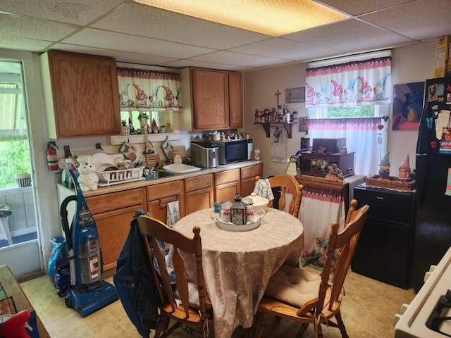 kitchen with a drop ceiling, stainless steel microwave, light countertops, brown cabinetry, and healthy amount of natural light