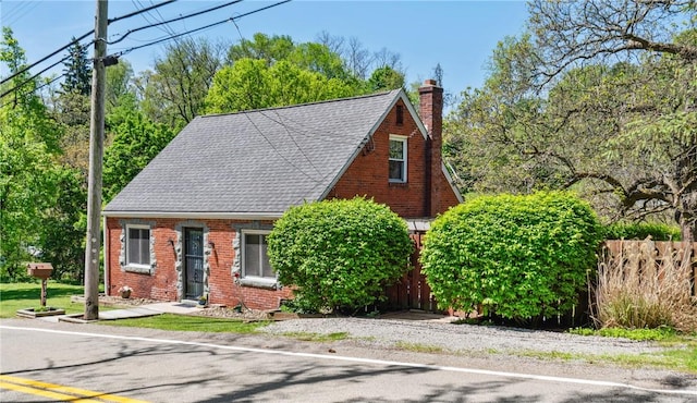 tudor house featuring a chimney, brick siding, and fence