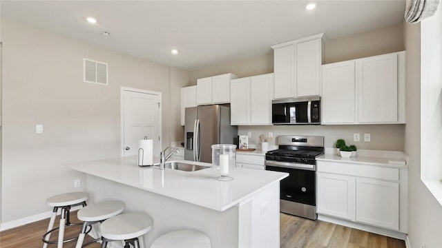 kitchen with appliances with stainless steel finishes, a sink, a center island with sink, light wood finished floors, and a breakfast bar