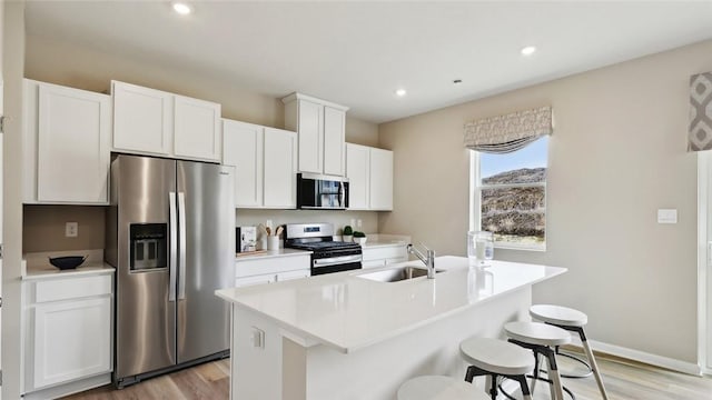 kitchen featuring appliances with stainless steel finishes, a sink, light wood-style flooring, a kitchen island with sink, and recessed lighting