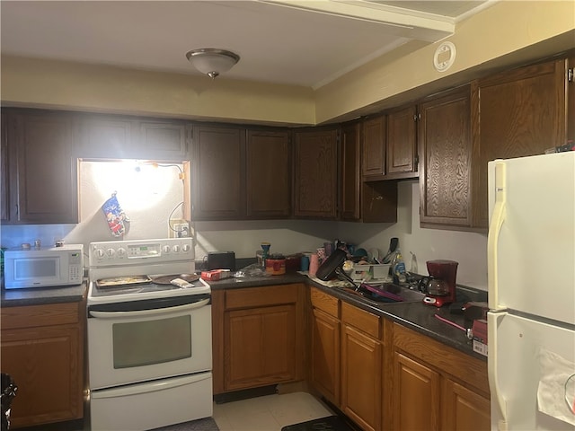 kitchen featuring white appliances, dark countertops, and a sink