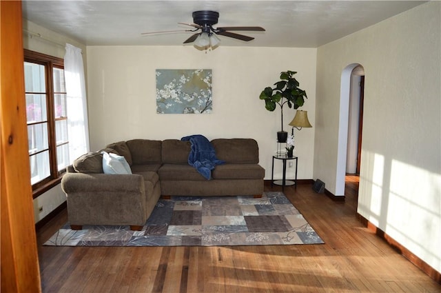 living room featuring arched walkways, ceiling fan, wood finished floors, and baseboards