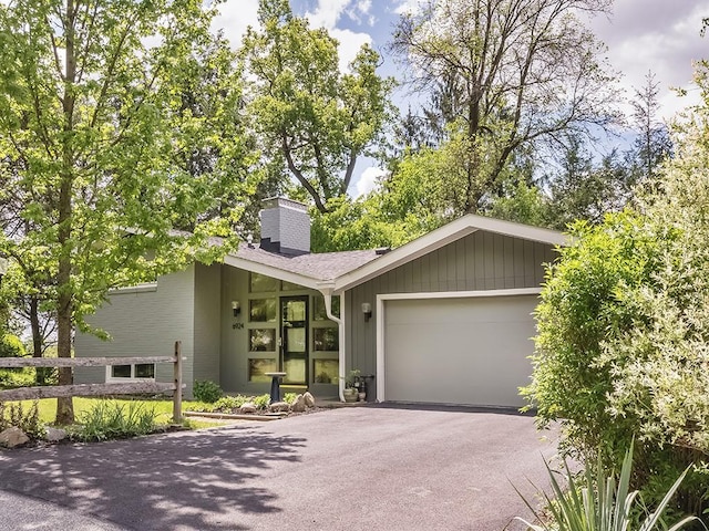 mid-century home featuring asphalt driveway, a garage, and a chimney