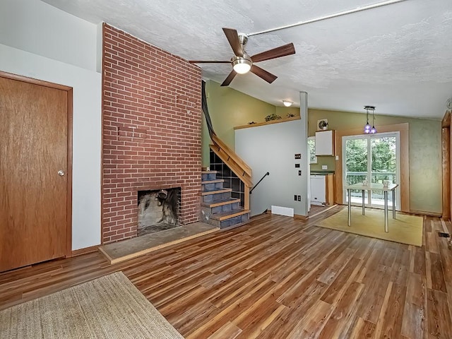 unfurnished living room featuring vaulted ceiling, wood finished floors, a ceiling fan, a textured ceiling, and a fireplace