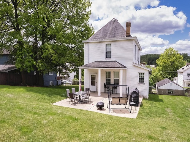 back of property with a chimney, a yard, a patio, and roof with shingles