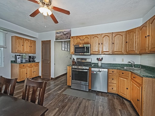 kitchen featuring appliances with stainless steel finishes, a sink, dark wood-type flooring, dark countertops, and a textured ceiling
