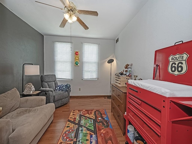 living area featuring ceiling fan, light wood-style flooring, and baseboards