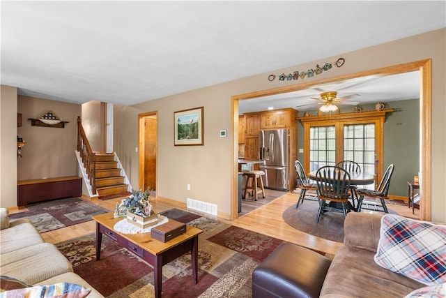 living area with light wood finished floors, baseboards, stairs, and ceiling fan