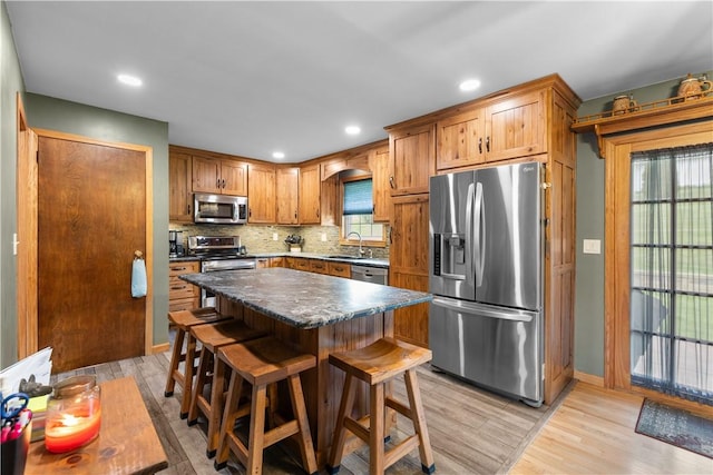 kitchen with stainless steel appliances, a sink, light wood-type flooring, tasteful backsplash, and dark countertops