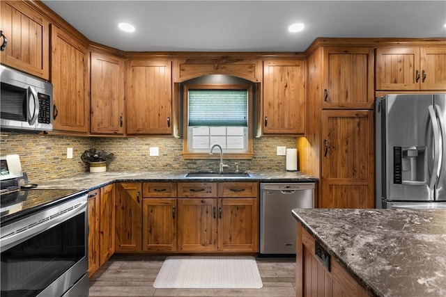 kitchen with appliances with stainless steel finishes, a sink, dark stone countertops, brown cabinets, and recessed lighting