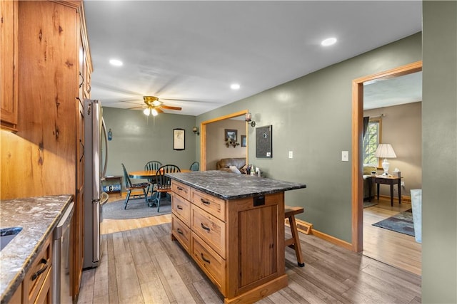 kitchen with a kitchen breakfast bar, light wood-style flooring, brown cabinetry, ceiling fan, and stainless steel appliances
