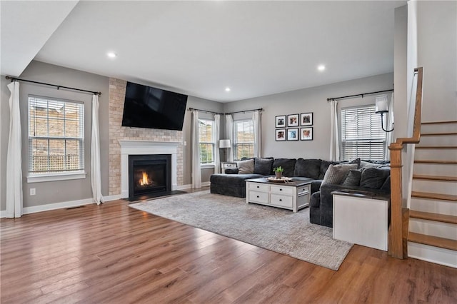 living area featuring wood finished floors, recessed lighting, baseboards, stairs, and a brick fireplace